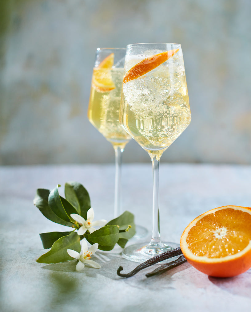 Two cocktail glasses filled with Everleaf’s Forest Spritz, surrounded by a wedge of orange, vanilla, saffron and orange blossom.