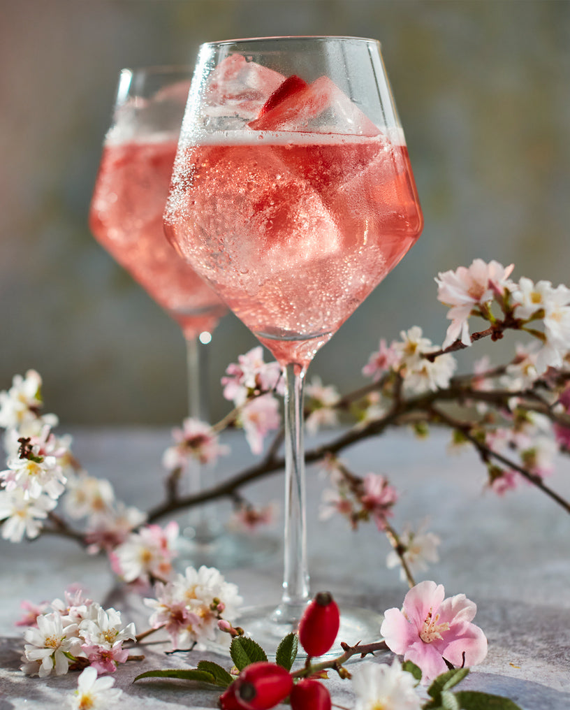 Two cocktail glasses filled with Everleaf’s Mountain Spritz, surrounded by a branch of cherry blossom leaves.